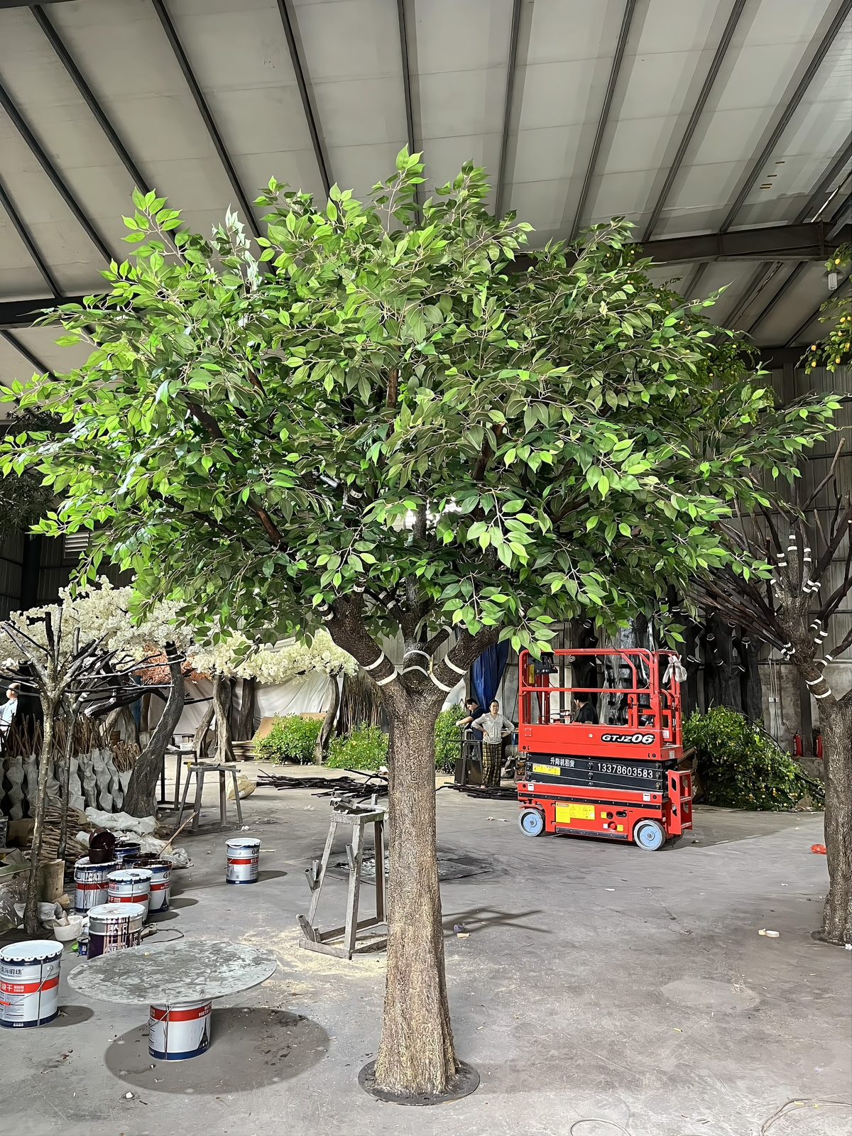 Large artificial ficus tree being finished in the workshop using a scissor lift