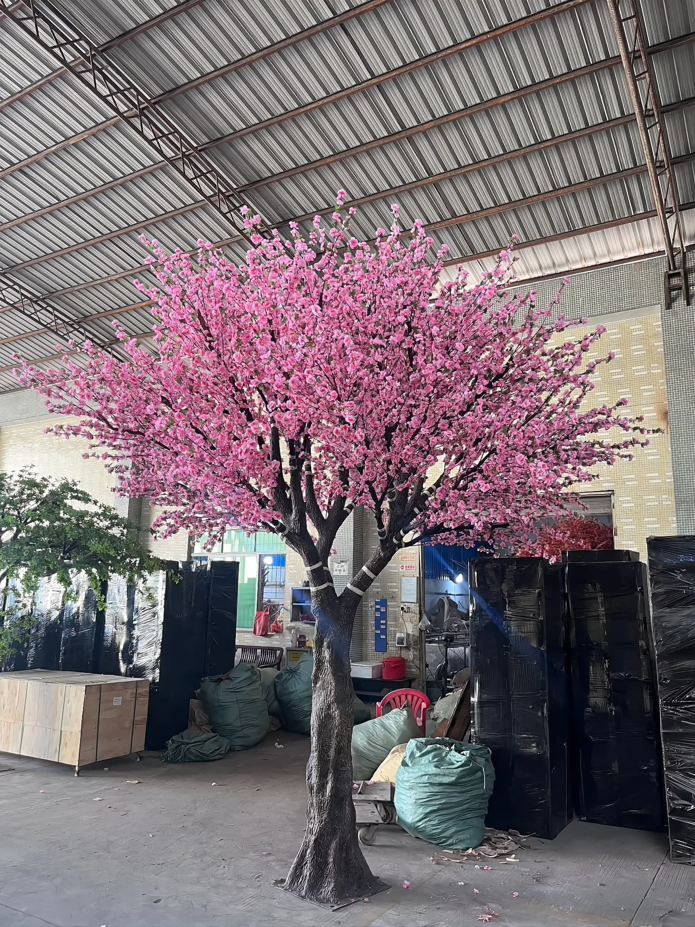 Full-size artificial cherry blossom tree with a dense pink canopy on the shop floor, checked at working height before crating