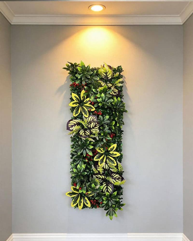 Compact indoor artificial foliage panel mounted on a grey wall under a warm downlight