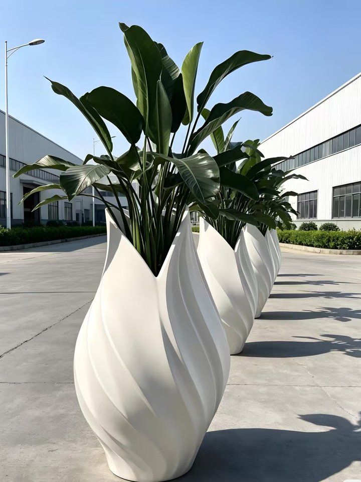 Three sculpted white fibreglass planters planted with artificial traveller's palm foliage, lined up in the Everflorae factory yard before packing